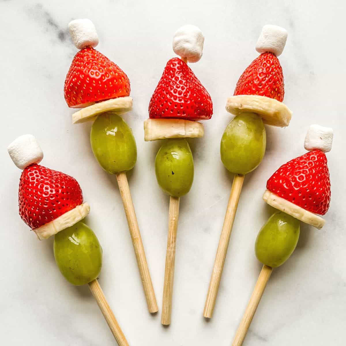 Grinch fruit skewers on a marble background.