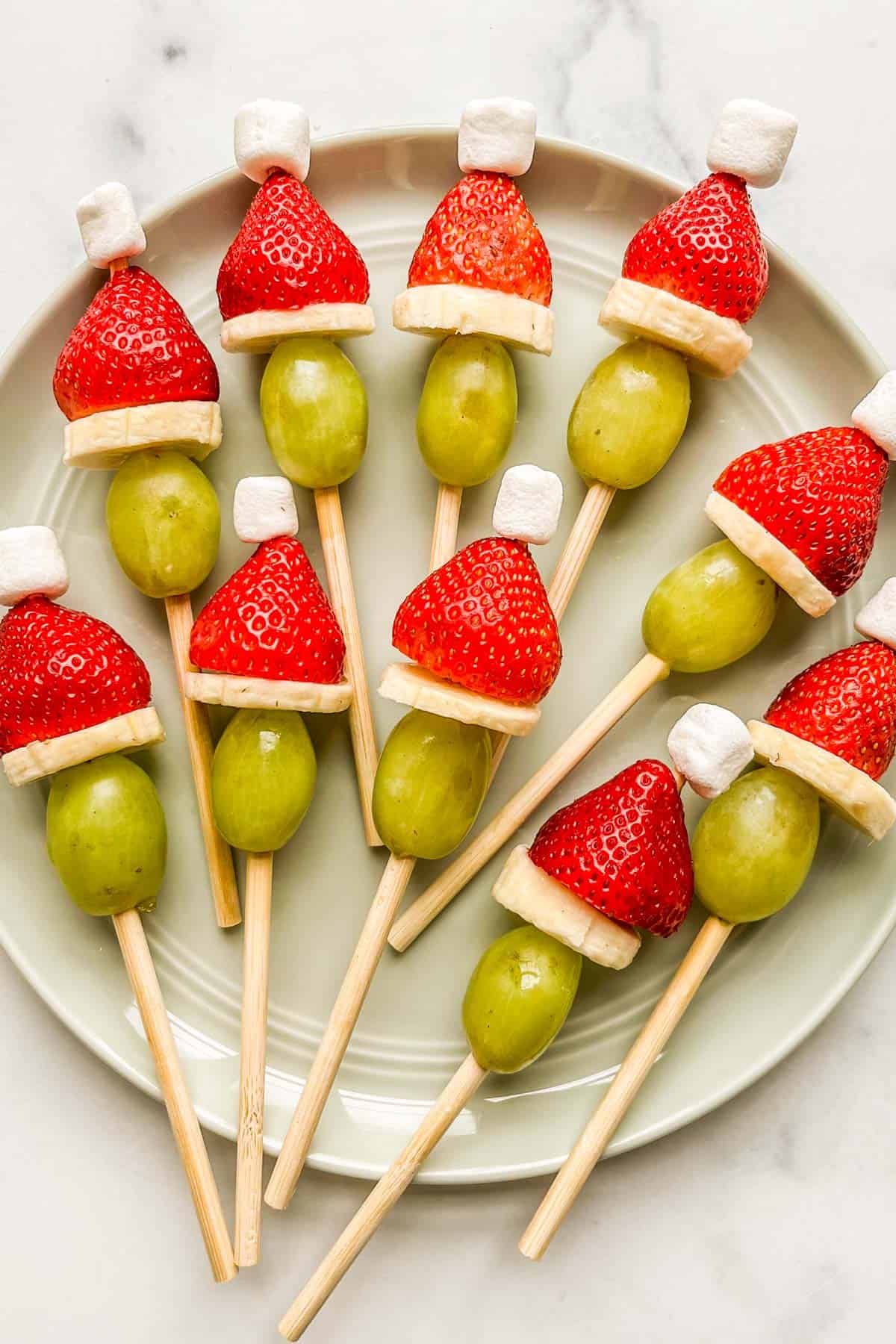 Grinch fruit kabobs on a green plate.