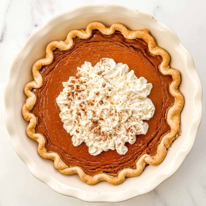 Healthy pumpkin pie topped with whipped cream in a pie plate.