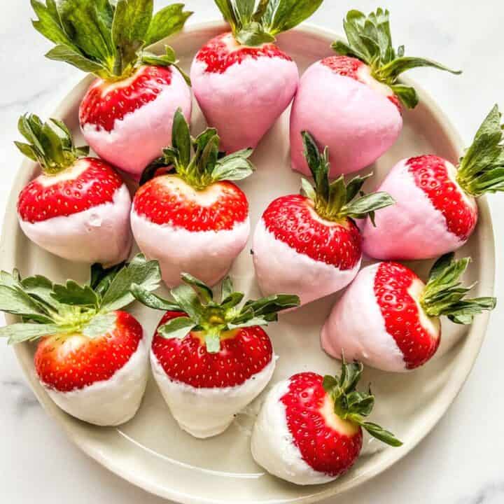 Pink yogurt covered strawberries on a white plate.