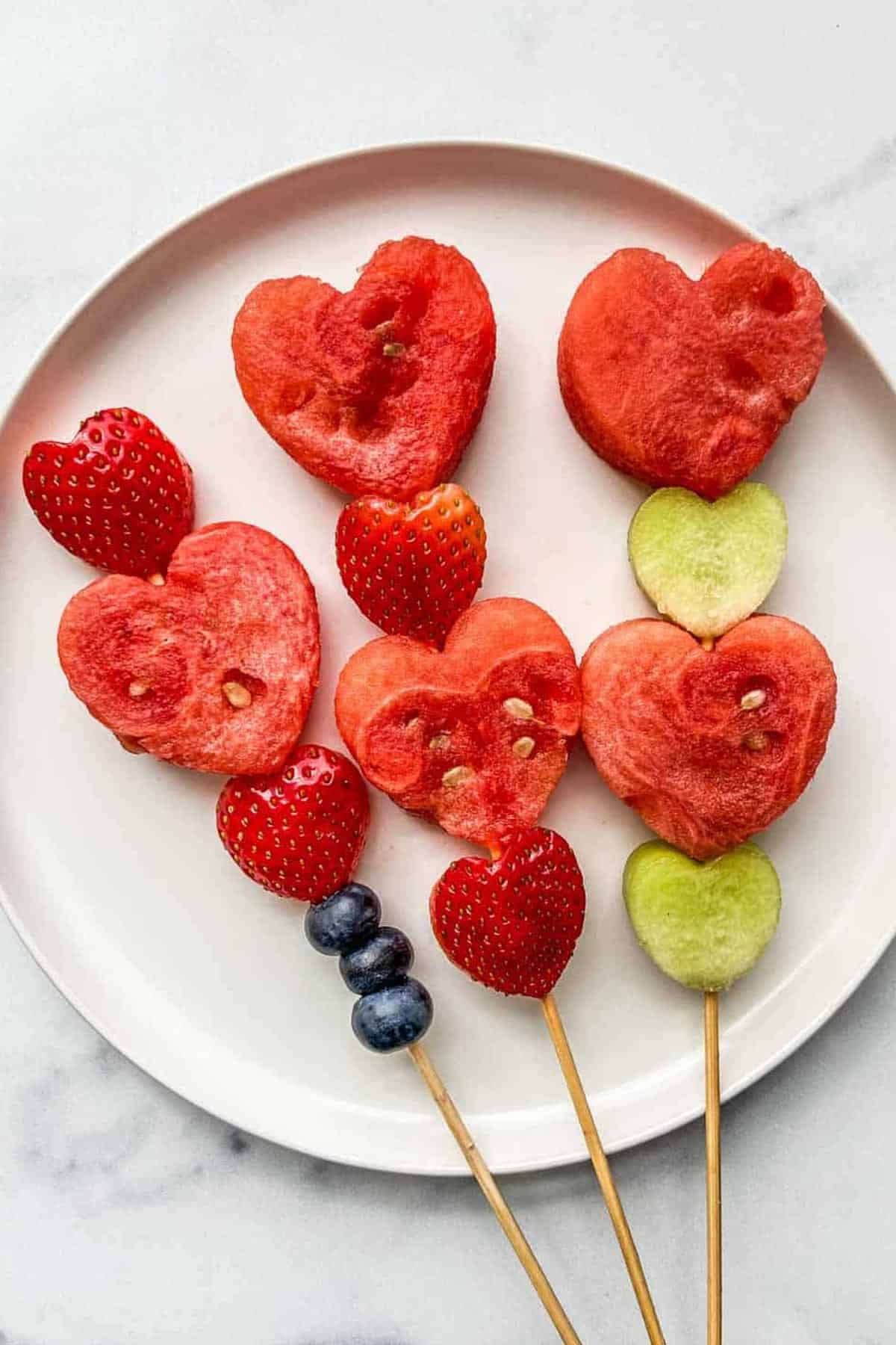 Valentine's fruit skewers on a white plate.