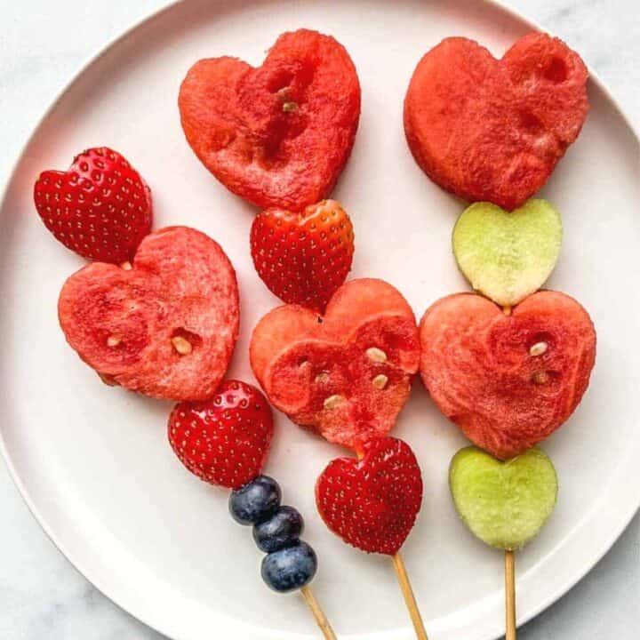 Heart fruit skewers on a white plate.