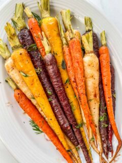 Roasted rainbow carrots with fresh herbs on a platter.
