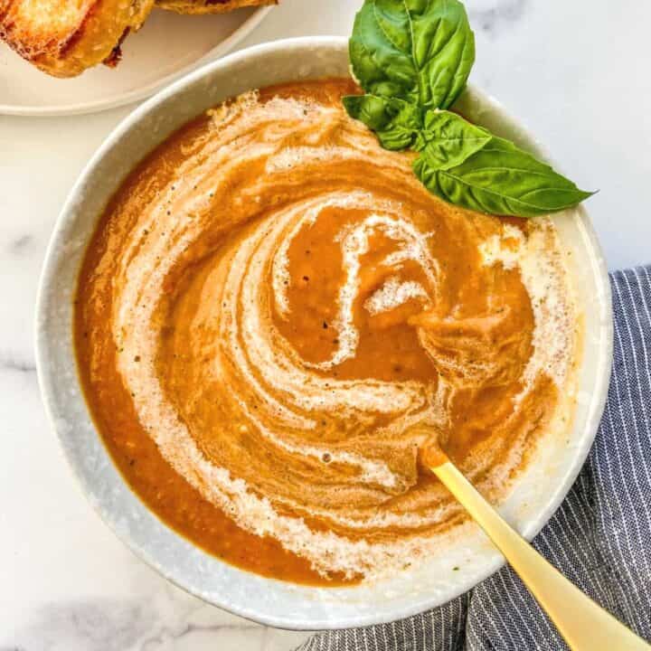 Roasted tomato soup with a cream swirl in a white bowl.