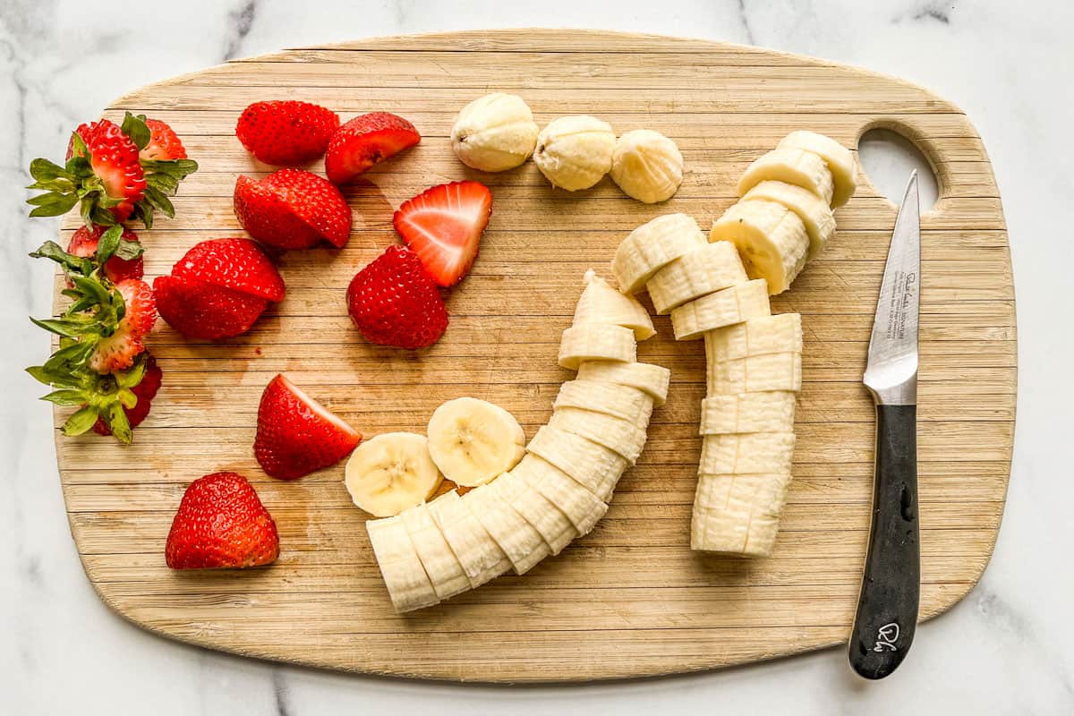 Sliced strawberries and bananas on a cutting board.