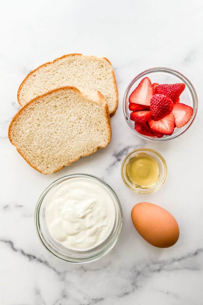 Two pieces of bread, yogurt, an egg, honey, and sliced strawberries.