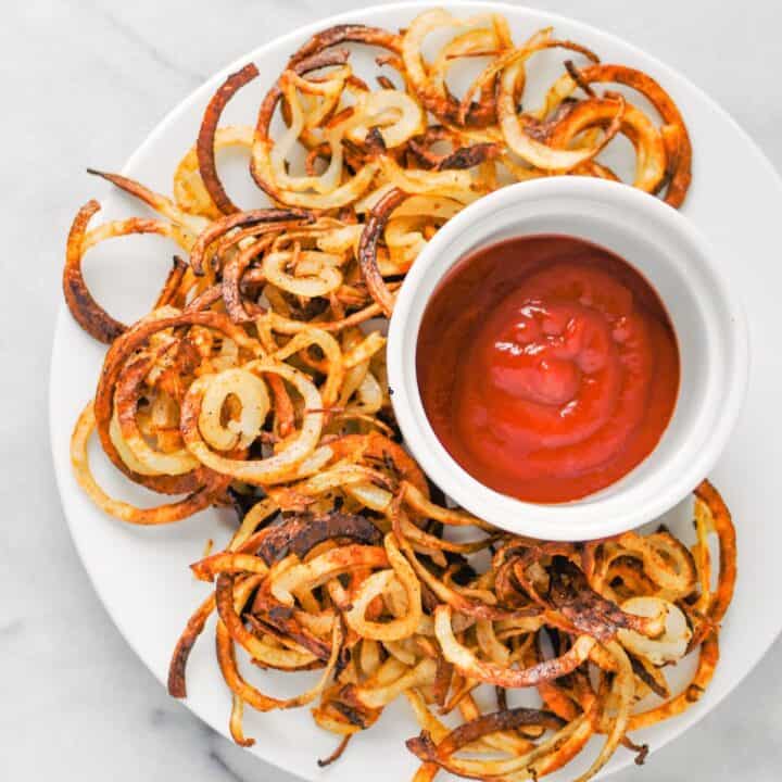 Baked curly fries with ketchup on a white plate.
