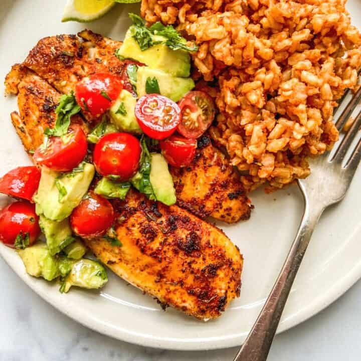 Blackened tilapia topped with tomatoes and avocados served with rice.