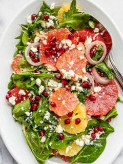 A citrus pomegranate salad on a large serving dish with serving spoon.