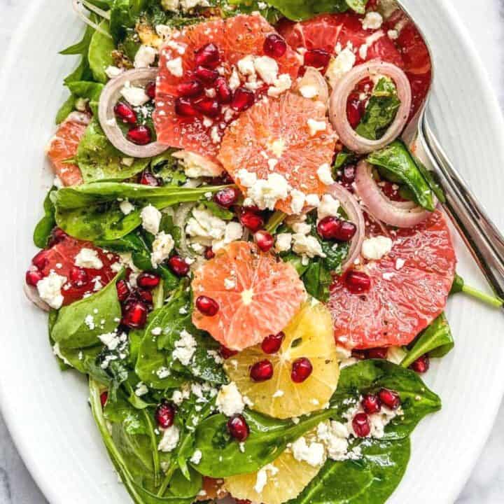 A citrus pomegranate salad with feta on a large white serving platter.