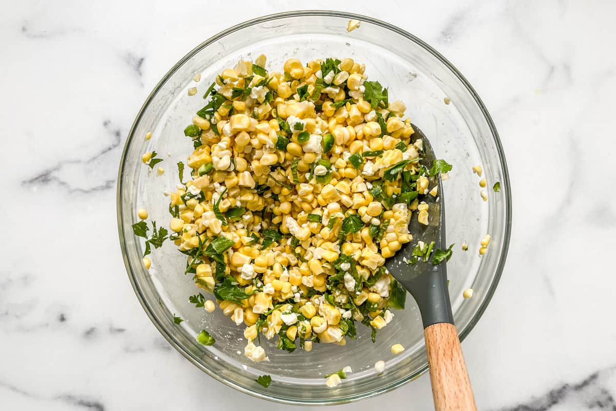 A corn and feta salad in a glass bowl.