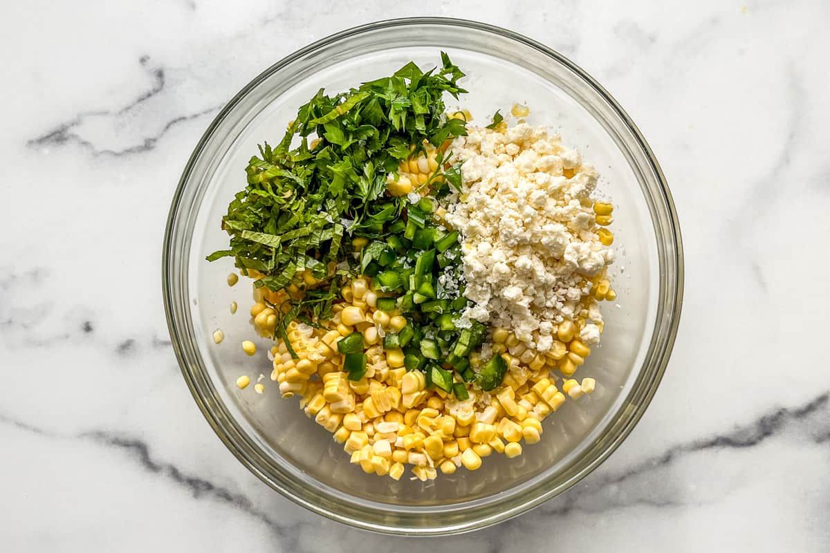 Sweet corn, jalapeno, herbs, and cheese in a glass bowl.