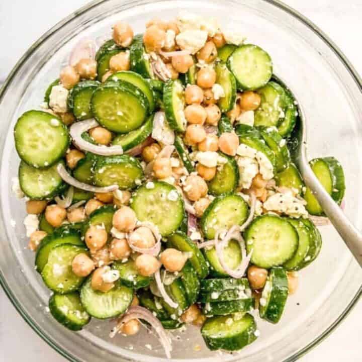 A chickpea cucumber salad with feta cheese in a glass mixing bowl.