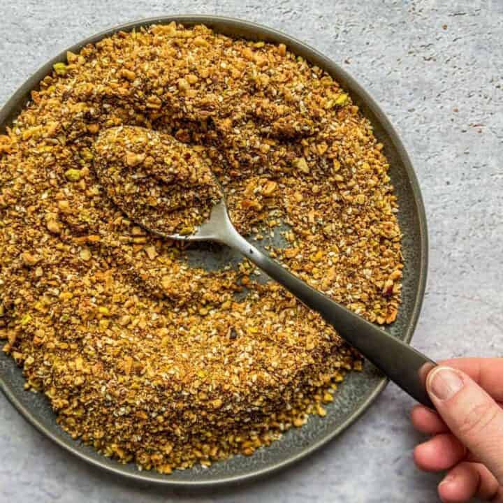 Dukkah spice on a metal plate with a spoon.