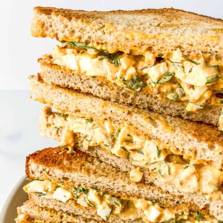 Egg salad sandwiches stacked on a plate.