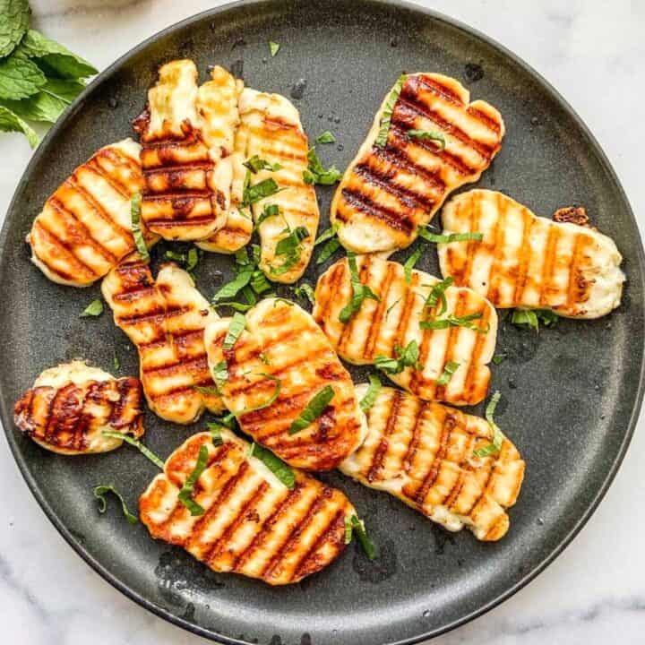 Grilled halloumi sliced on a black plate.