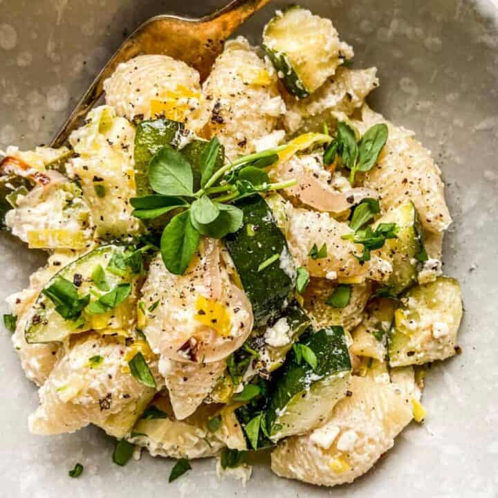 A healthy pasta recipe with zucchinis in a speckled bowl.