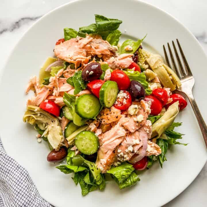 A white plate with salmon Mediterranean salad.