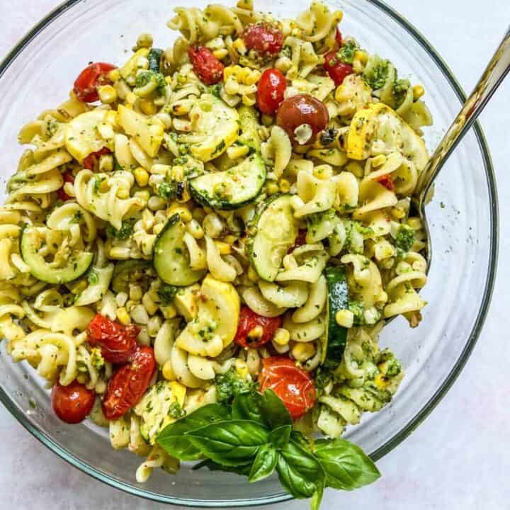 Pesto pasta salad in a bowl with tomatoes and zucchini.