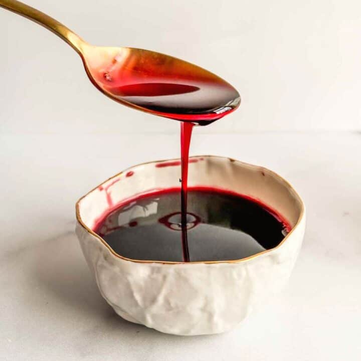 Pomegranate molasses dripping off a gold spoon into a bowl.