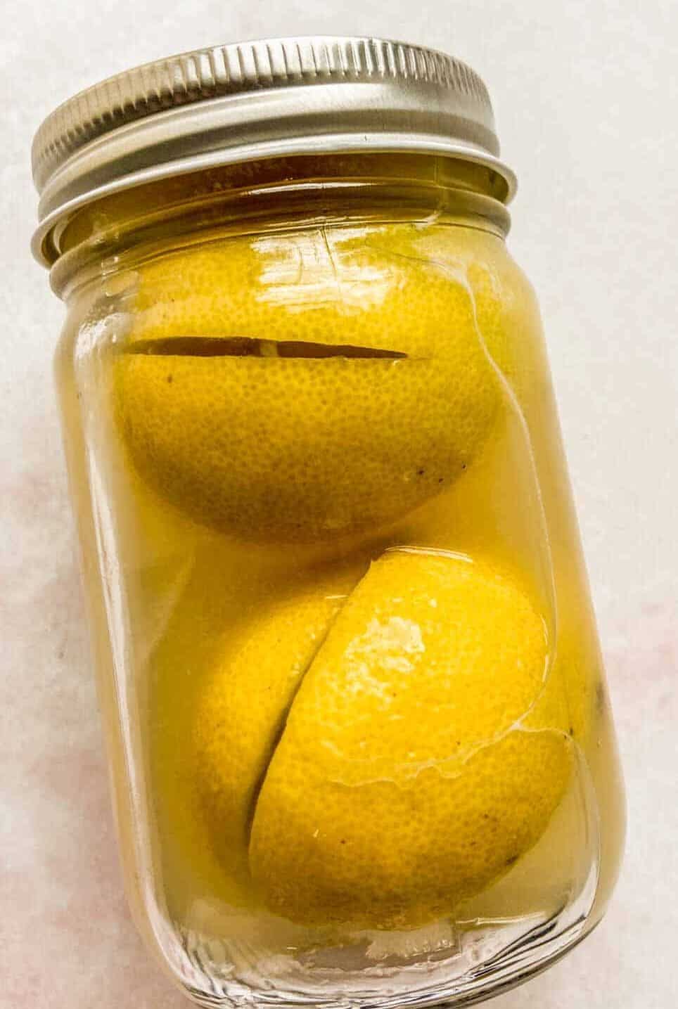 A glass jar with two preserved lemons.