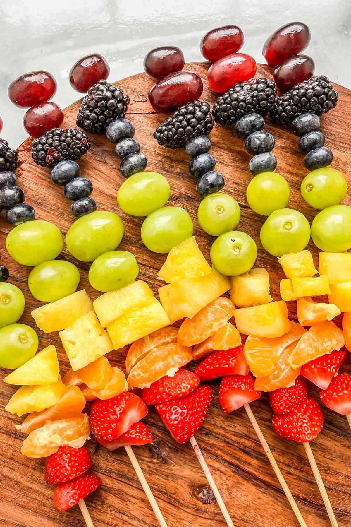 Rainbow fruit skewers on a wooden plate.