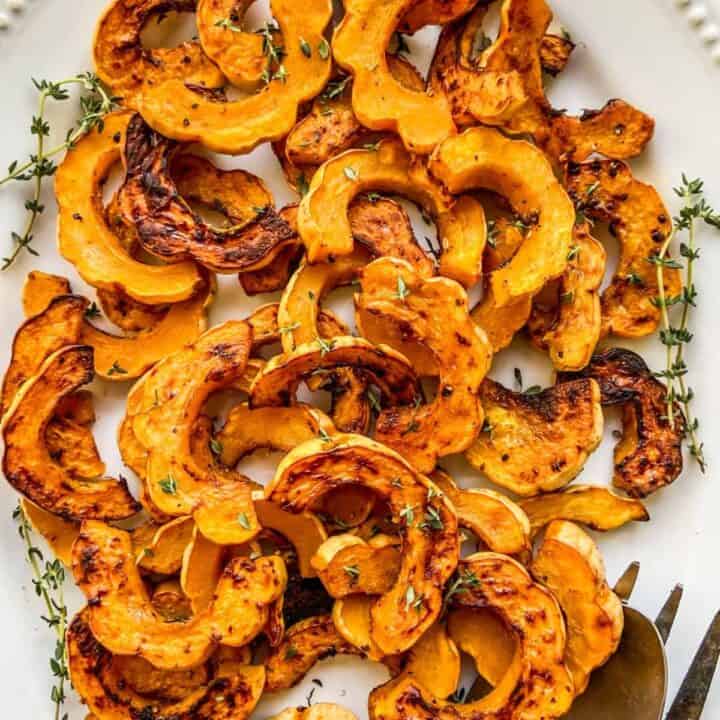 Roasted delicata squash topped with herbs on a platter.