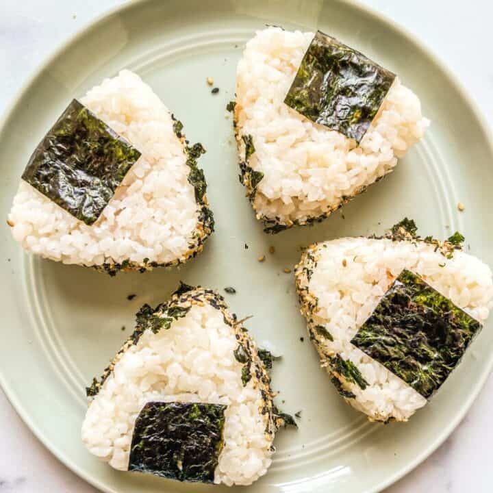 Four spicy tuna onigiri on a green plate.