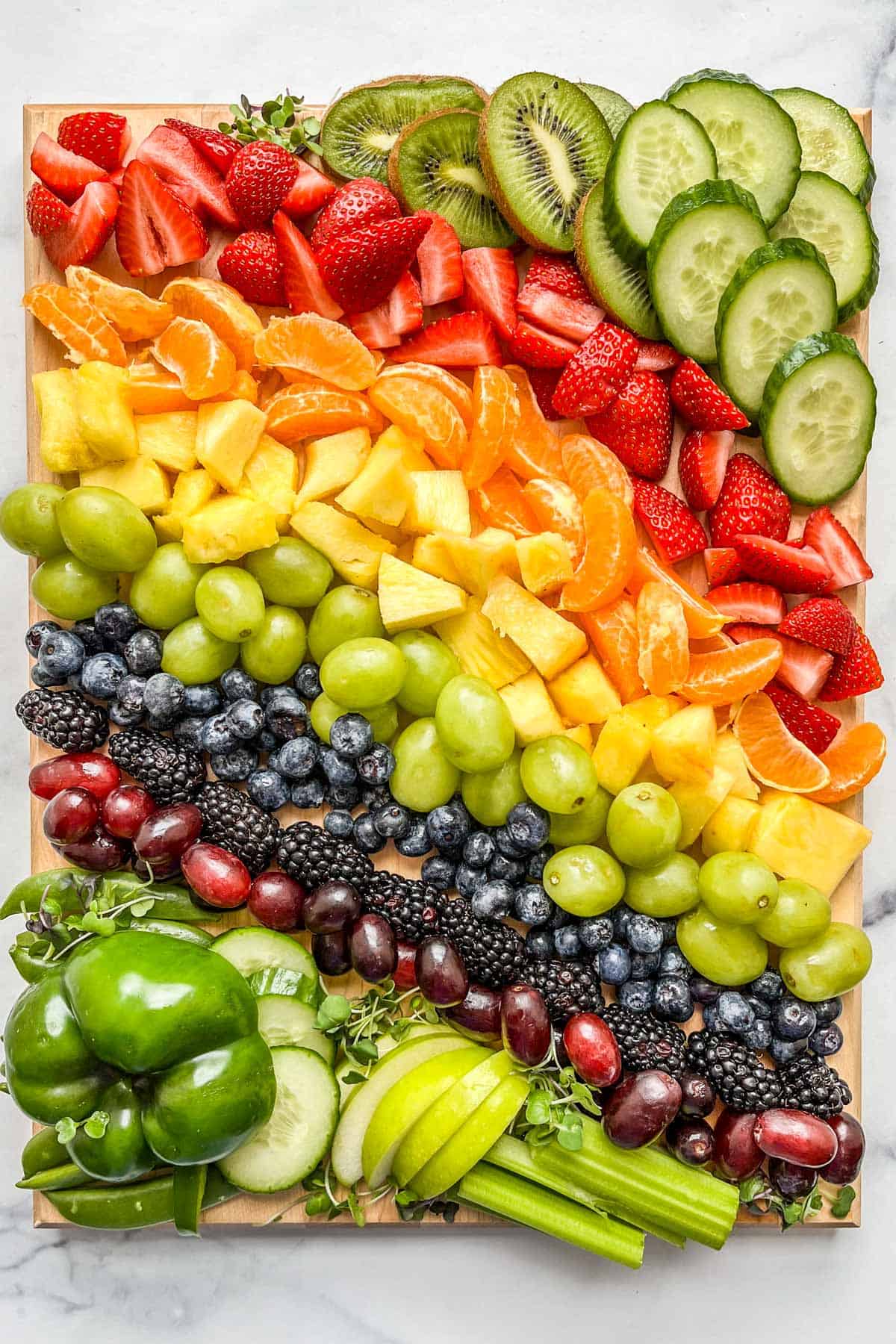 A St. Patricks Day appetizer board with rainbow fruit and green vegetables.