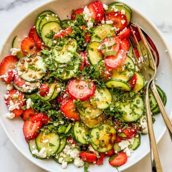 A strawberry cucumber salad in a white serving bowl.