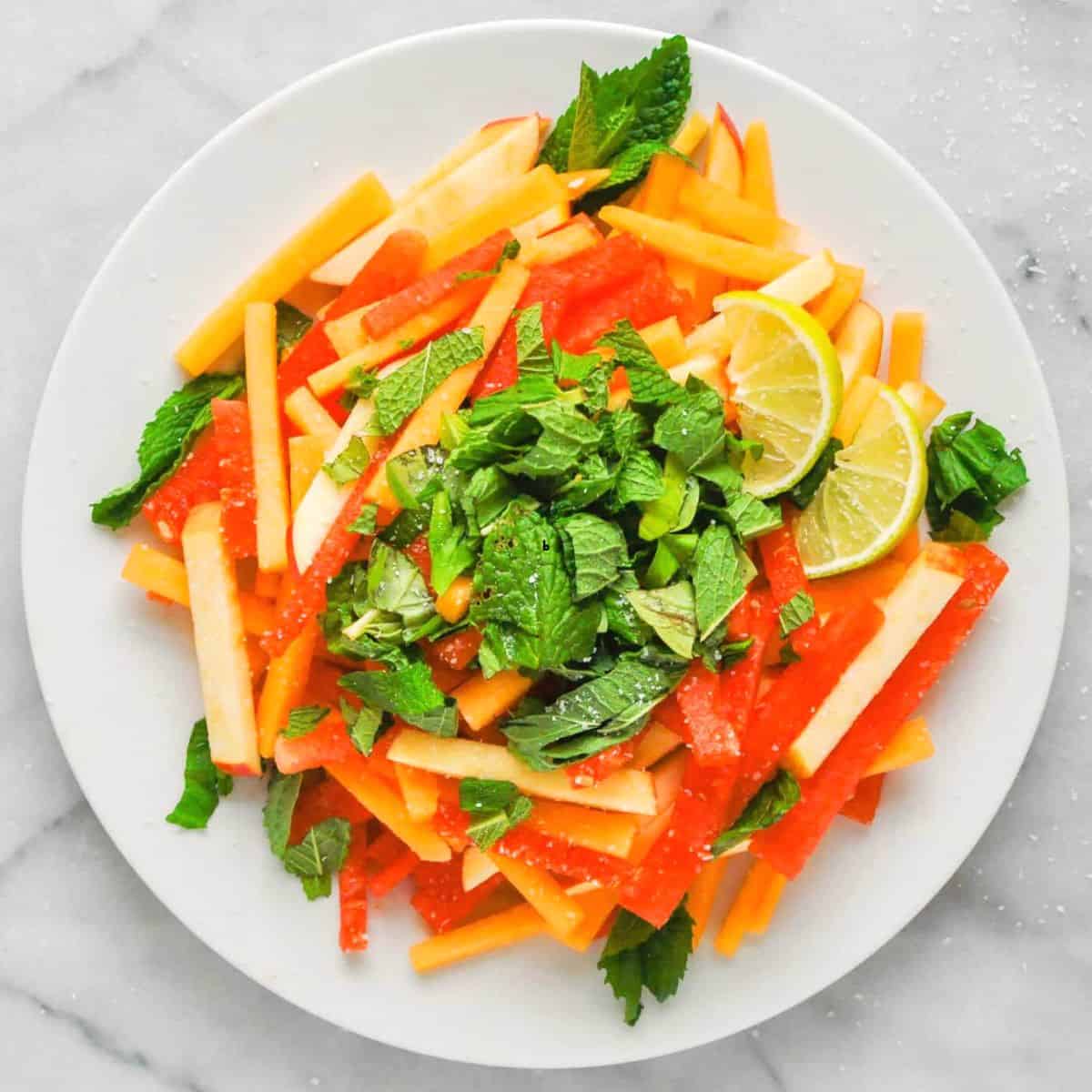 Watermelon apple and cantaloupe salad on a white plate.