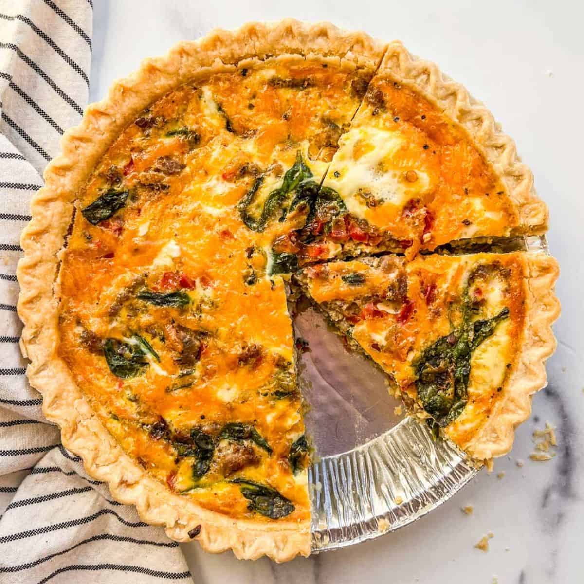 A breakfast quiche in a metal pan next to a striped dishcloth.