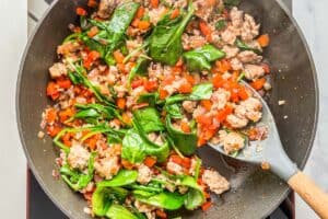 Breakfast sausage, spinach, bell pepper, onion, and garlic being simmered in a pan.