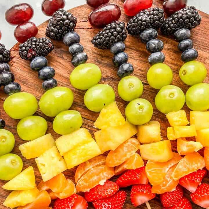 Rainbow fruit skewers on a wooden platter.