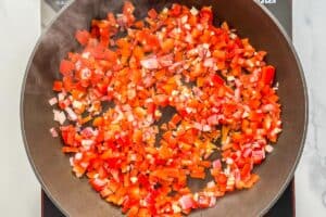 Bell pepper, red onion, and garlic being sautéed in a pan.