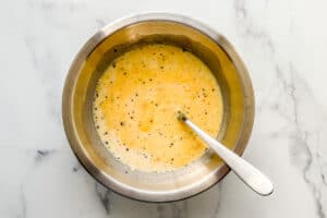 Eggs, cheese, milk, salt and pepper whisked in a bowl.