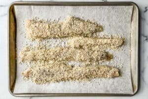 Panko parmesan pollock fillets on a baking sheet before going in the oven.