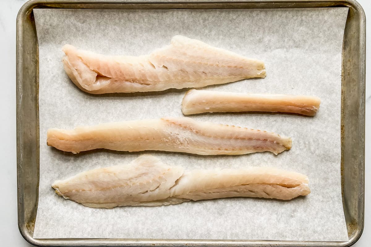 Pollock fillets on a parchment lined baking sheet.