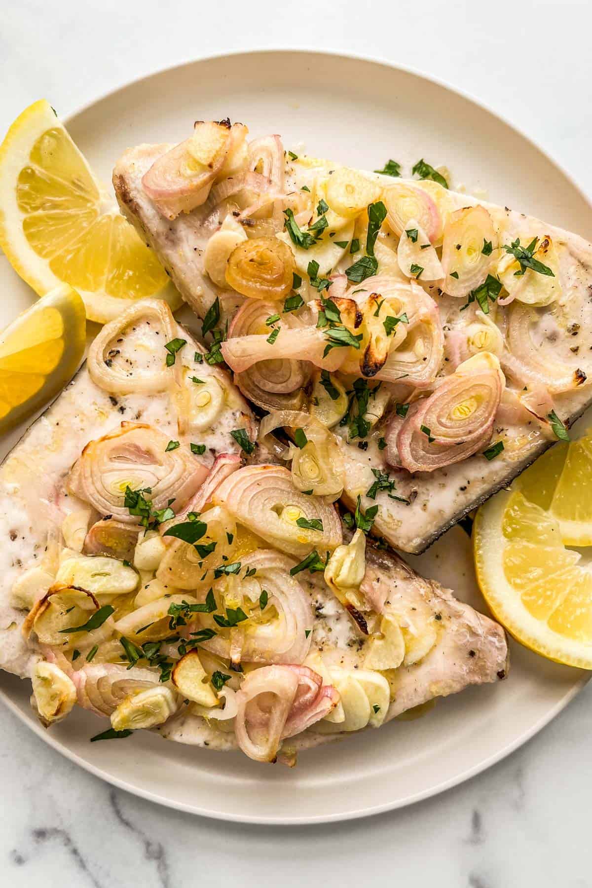 Baked swordfish with lemon and shallots on a white plate.