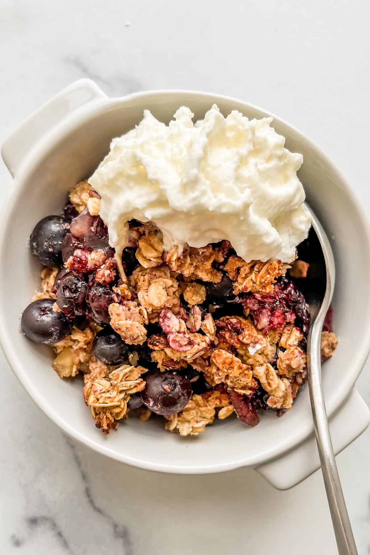 A ramekin with blueberry crisp and whipped cream.