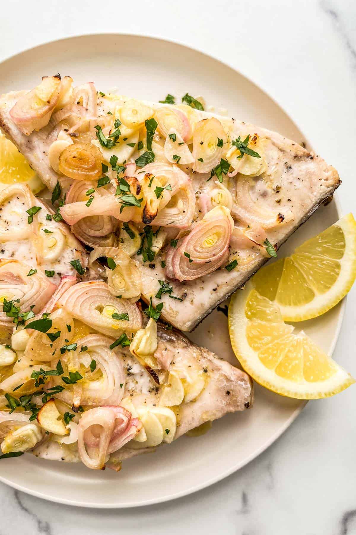 Lemon baked swordfish on a white plate.