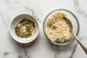 A small bowl with an herb and spice blend and a glass bowl with panko and parmesan cheese.