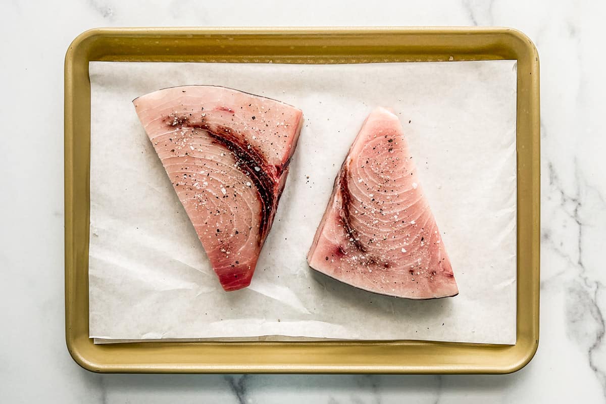 Two swordfish steaks on a parchment-lined rimmed baking sheet.