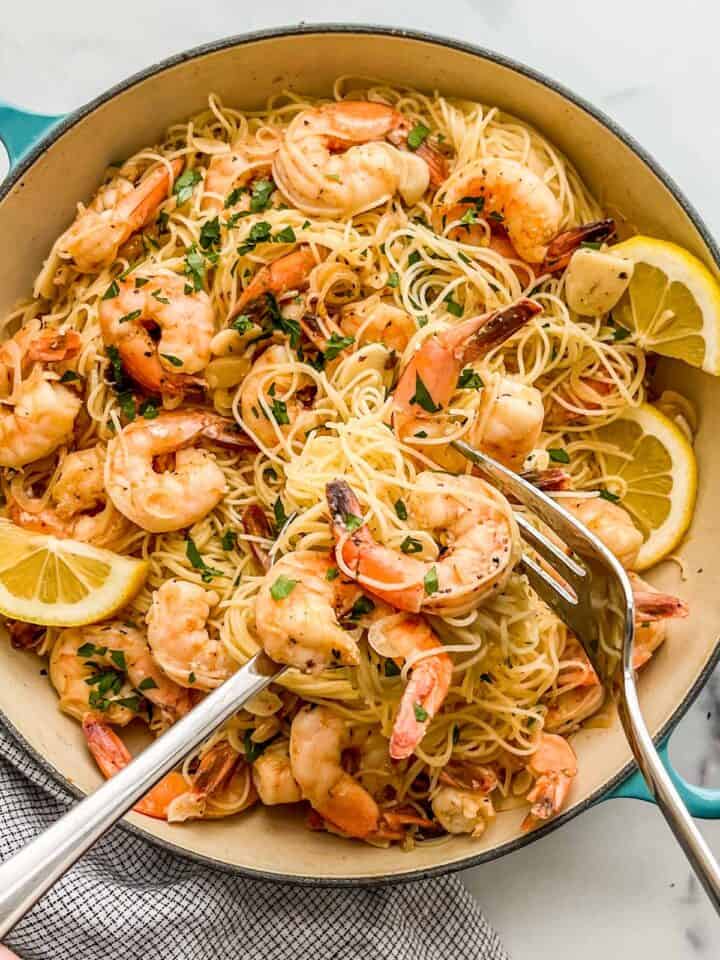 Shrimp angel hair pasta in a skillet with a large serving fork and spoon.