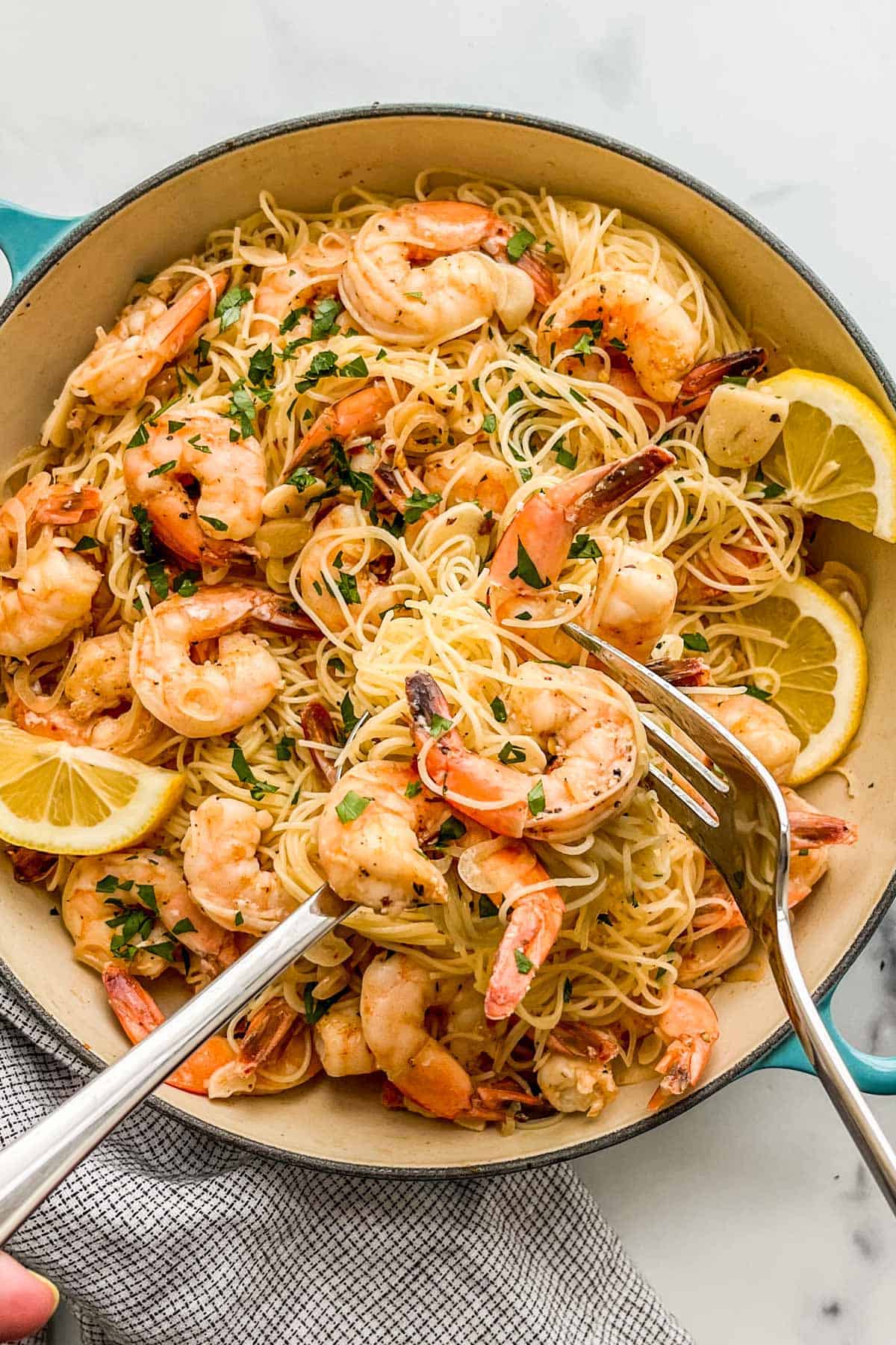 Shrimp angel hair pasta in a skillet with a large serving fork and spoon.