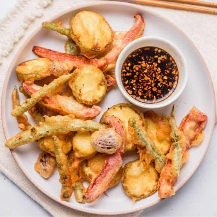 Tempura vegetables with dipping sauce on a white plate.