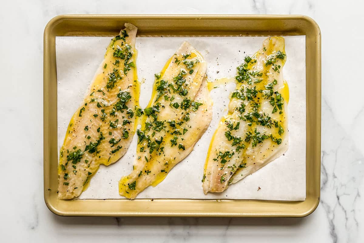 The sole fillets on a baking sheet topped with the lemon parsley sauce.