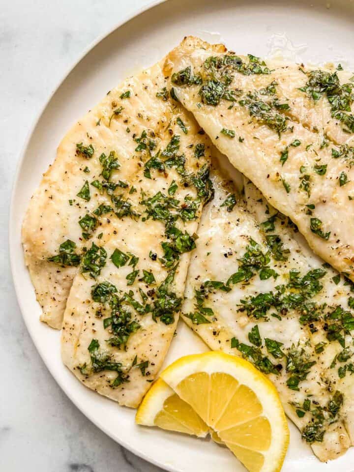 Baked sole fillets on a white plate with lemon slices.