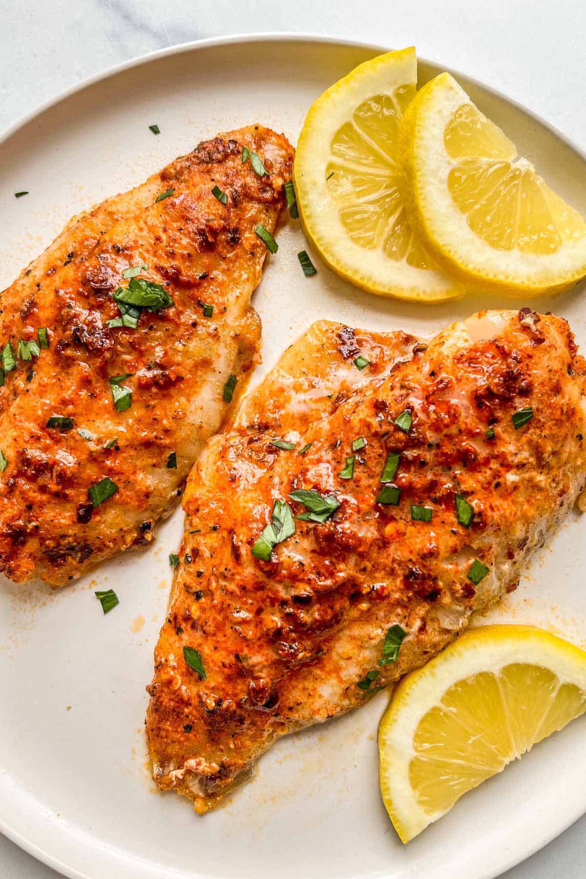 Two pieces of baked perch with lemon slices on a white plate.