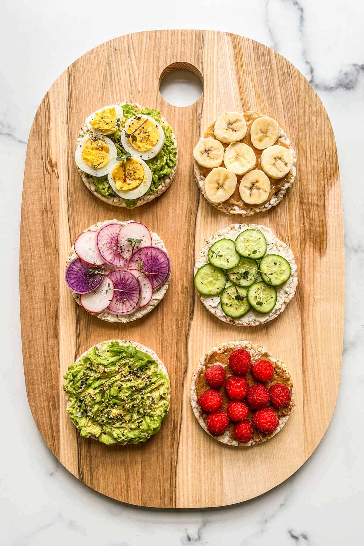 Six rice cakes with different toppings on a cutting board.